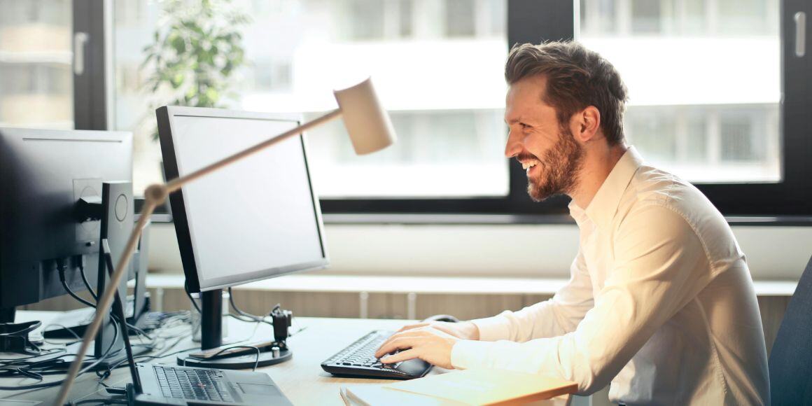 Office worker smiling in front of his computer managing inventory accuracy.