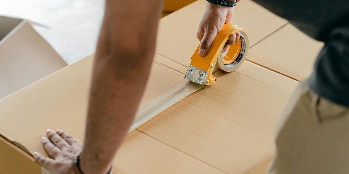 Man closing a box with tape to fullfill an omnichannel ecommerce experience.