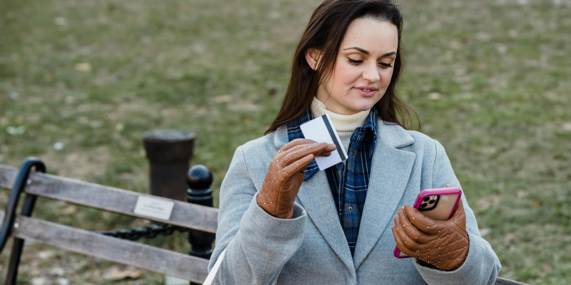 Woman dressed in winter coat holds her card and phone having an omnichannel ecommerce experience.