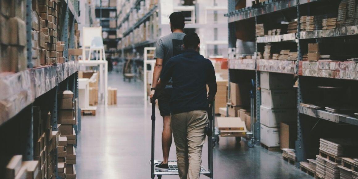 Two workers in a warehouse pushing a cart through the aisle, illustrating fulfillment efficiency.